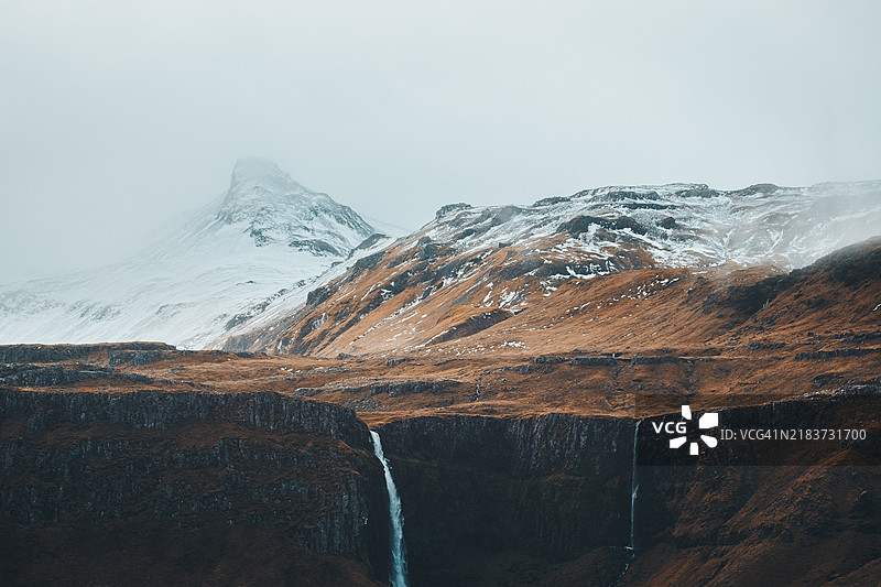 格伦达尔瀑布在冰川山峰的背景下倾泻而下，冰岛图片素材