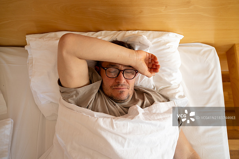 成熟男性因疼痛躺在床上，盖着毯子。忧郁的心情，心理健康。生活问题图片素材