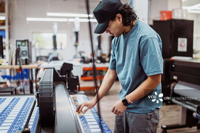 男性工人在工厂操作大幅面打印机和切纸机图片素材