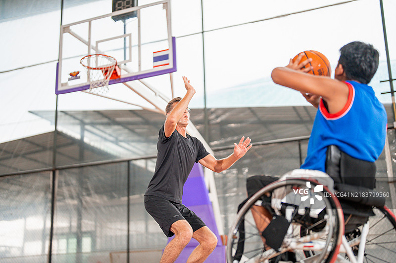一名坐在轮椅上的男子可以和朋友们在运动场上打篮球。图片素材
