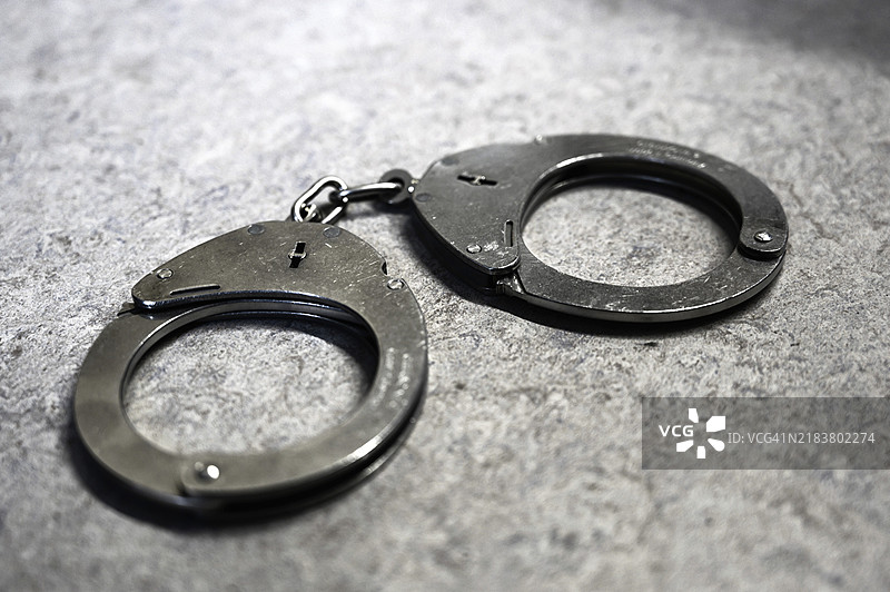 银色手铐在灰色背景上象征着犯罪行为图片素材