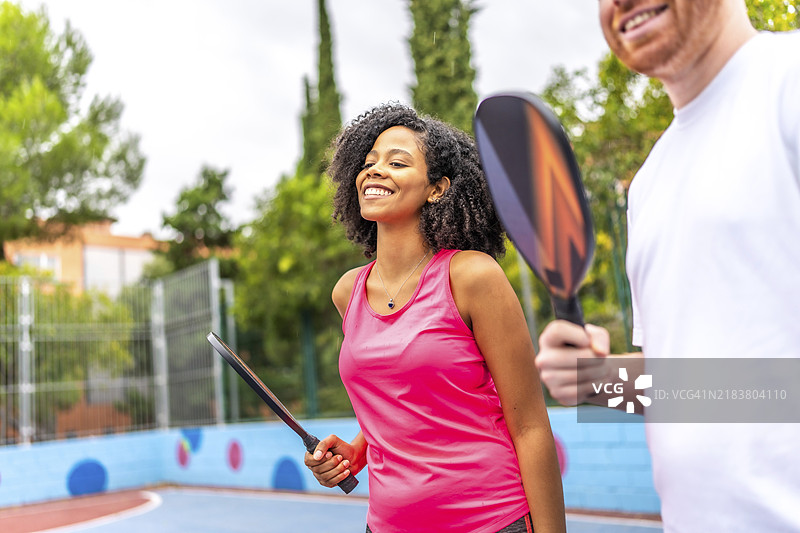 拉丁裔女性在户外城市球场与白人男性朋友微笑着打皮克球图片素材