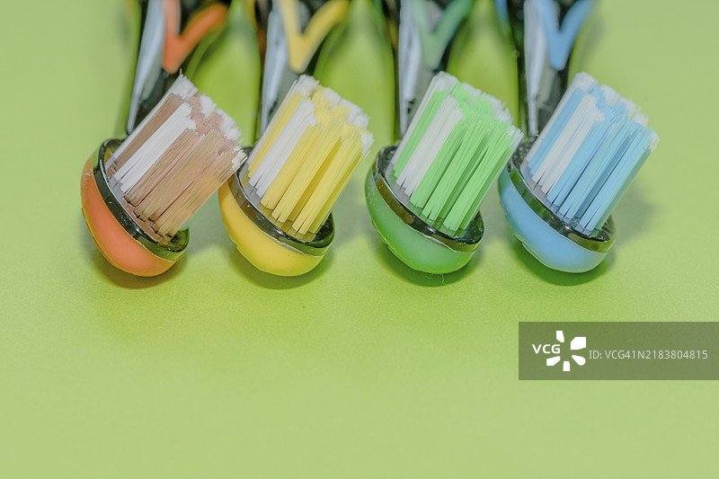 四把橙色、黄色、绿色和蓝色的牙刷特写，背景为绿色。图片素材