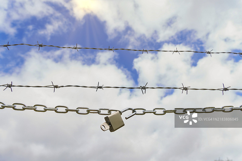 带锁链的锁打开，旁边有钥匙和带刺铁丝网，蓝天白云中透出阳光，象征自由的概念图片素材