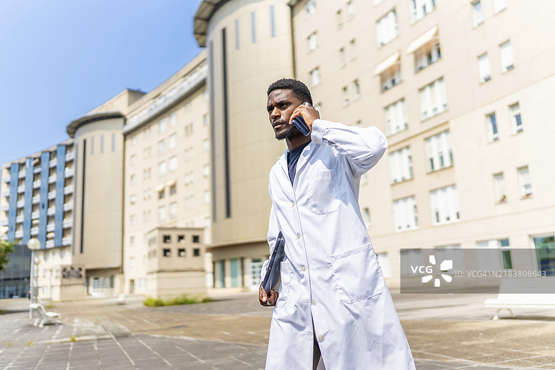 忙碌的非洲医生在医院外面走着，面带严肃表情与手机通话图片素材