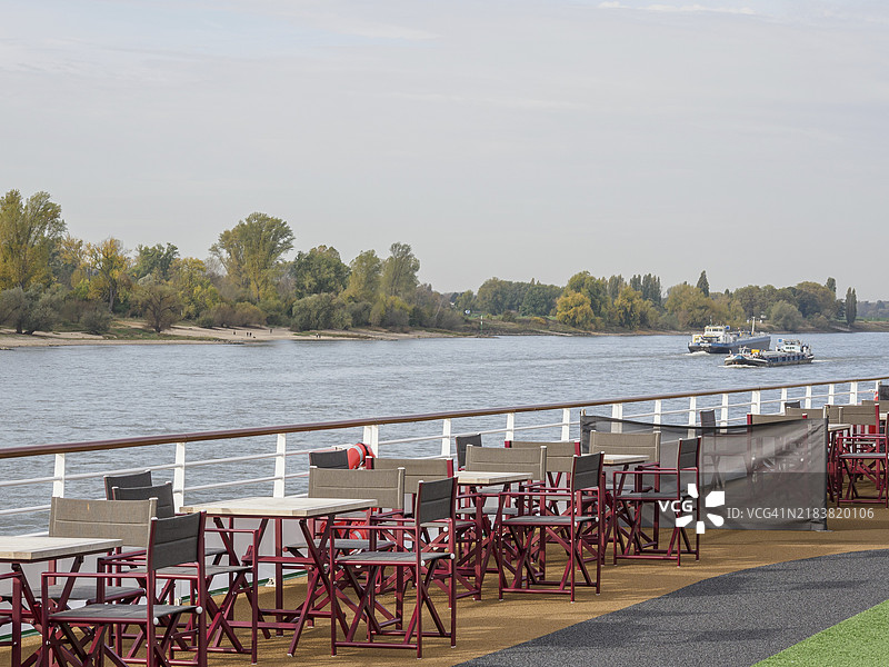 船甲板上的空座位区，俯瞰着河流和秋季河岸风景，莱茵河的秋季氛围，树上的秋叶和河上的船只，德国杜塞尔多夫，欧洲图片素材