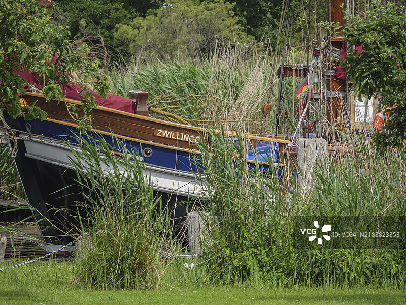 一艘名为“Zwilling”的帆船在高草和树木环绕的自然环境中可见，地点为德国吕贝克的特拉维缪德。图片素材