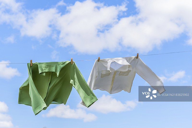 阳光下晾晒的衬衫在空中飘动，背景是蓝天和白云。图片素材