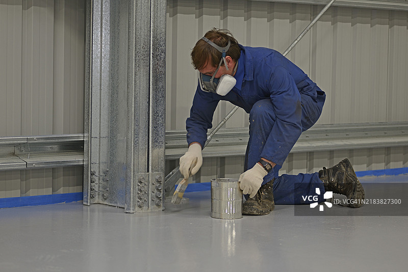 一名工匠在墙边涂抹环氧地坪材料，而其他团队成员则使用滚筒完成工作。图片素材