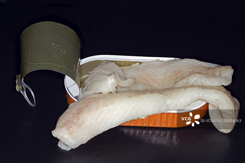 大西洋鳕鱼（Gadus morhua）片，斯克雷，放置在打开的铝罐中，黑色背景的摄影作品图片素材