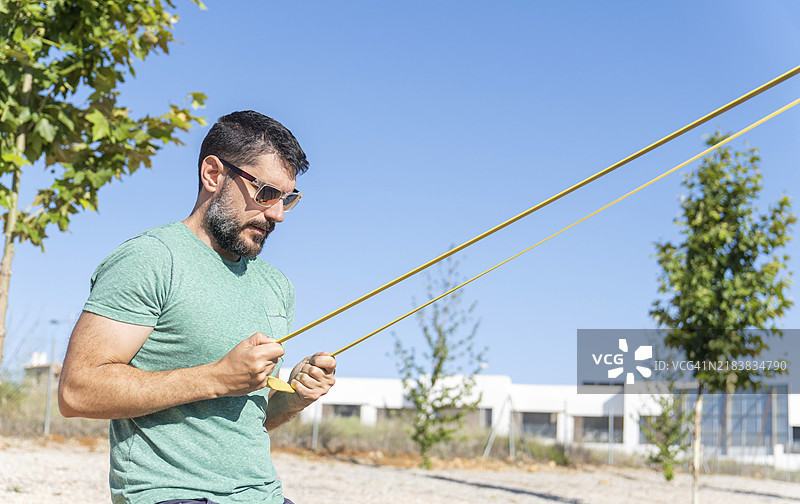戴着太阳镜的胡子男人侧身在户外健身房用弹性健身带训练二头肌图片素材