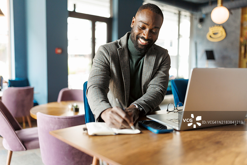 勤奋的男人在使用笔记本电脑时写笔记。图片素材
