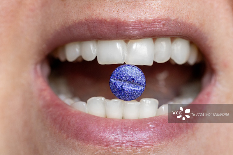 女人牙齿间夹着一颗紫色药丸的特写镜头图片素材