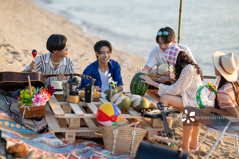 一群朋友在海滩的篝火派对上愉快地享受时光，背景是落日。图片素材