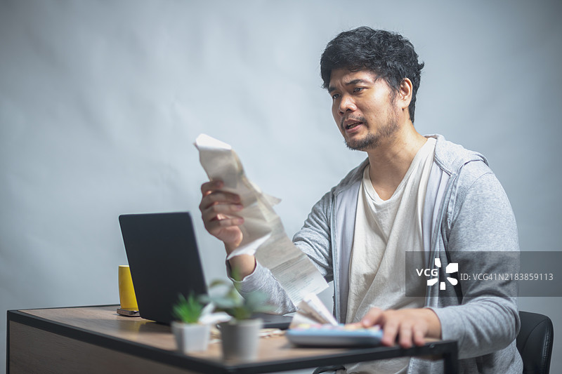 一名男子坐在桌子前，面露困惑地审阅文件，面前放着一台打开的笔记本电脑和一杯果汁。图片素材