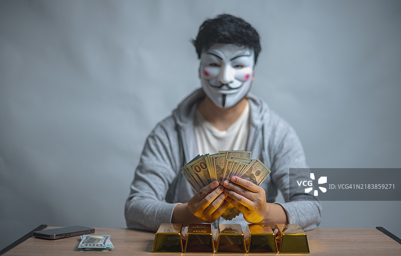 戴着盖伊·福克斯面具的人在桌子上数着一叠钱，象征着匿名性和潜在的非法金融活动。图片素材