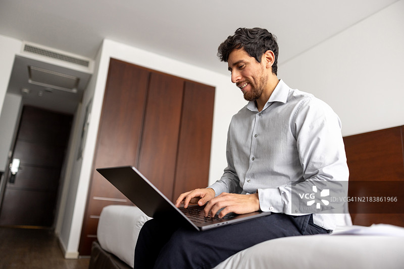 快乐的男士在酒店房间里出差时使用笔记本电脑工作图片素材