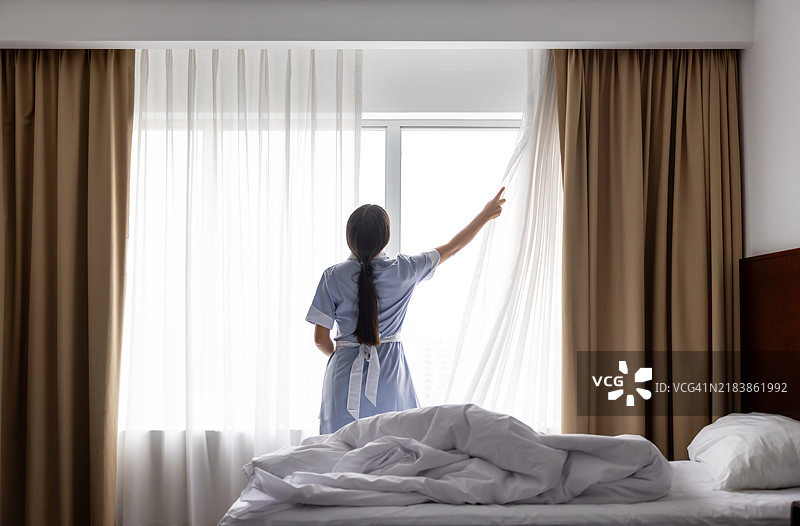 女仆在清理酒店房间并拉开窗帘图片素材