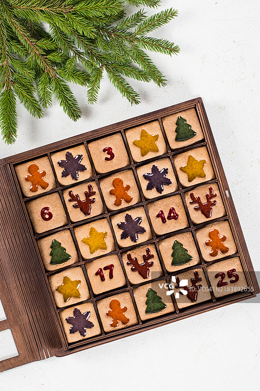 25个圣诞倒计时日历饼干。姜饼饼干，里面填充五彩缤纷的果酱，形状有姜饼人、星星、圣诞树、雪花、鹿头和数字。放在一个木制节日盒子里。俯视图。图片素材