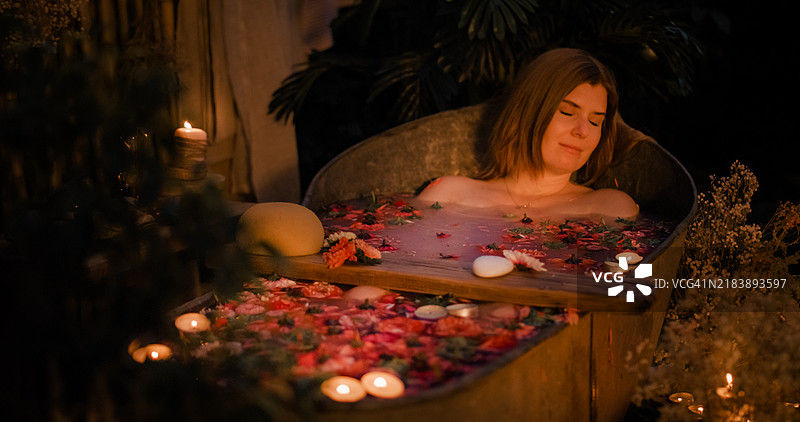 一位女性在花园里的锌浴缸中放松，周围有许多蜡烛。图片素材