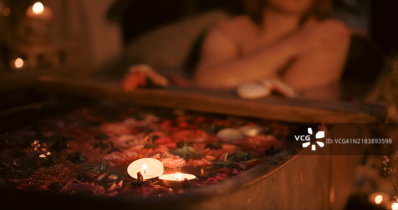 一位女性在花园中的锌浴缸里放松，周围有许多蜡烛。图片素材