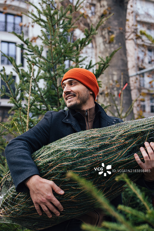 男人在城市环境中快乐地搬运圣诞树图片素材