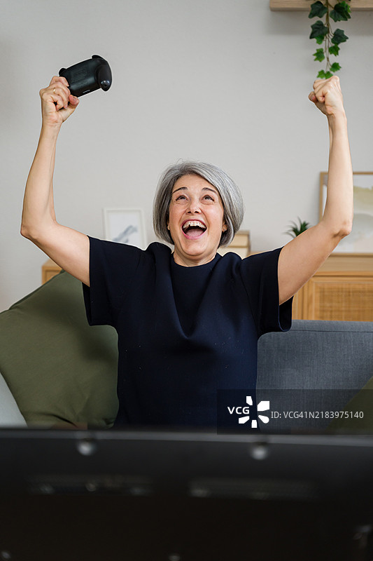 兴奋的老年女性在家沙发上赢得电子游戏图片素材