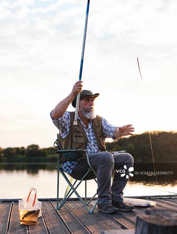 祖父在日落时分的宁静湖泊钓鱼图片素材
