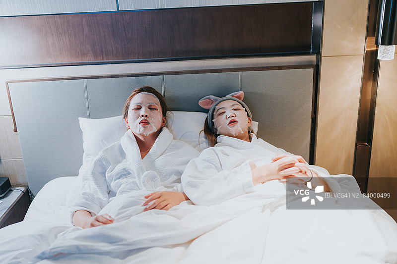 快乐的Z世代女孩们在中国大湾区珠海旅行。她们脸上戴着面膜，正在酒店房间的床上休息。图片素材