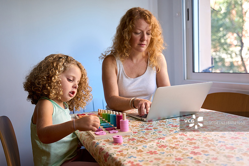 母亲在家工作，女儿在玩教育玩具图片素材