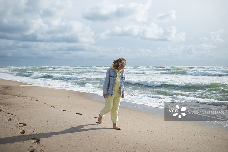 女孩在海滩上行走，强风吹拂。图片素材