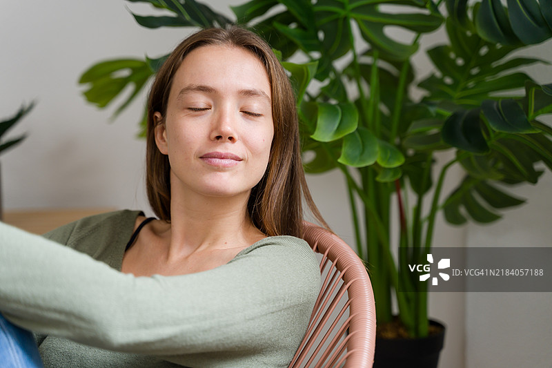 宁静的女性在家中放松，闭着眼睛，享受与室内植物相伴的宁静。图片素材