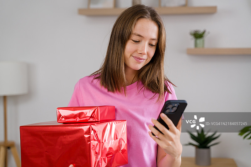 年轻女性在家中手持礼物并使用智能手机图片素材