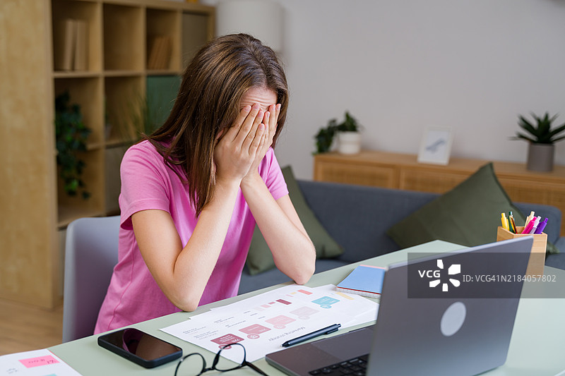 在家办公桌前，压力重重的女商人用双手捂住脸。图片素材