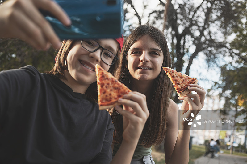 阳光明媚的夏日，快乐的男孩和女孩在户外吃披萨并自拍图片素材