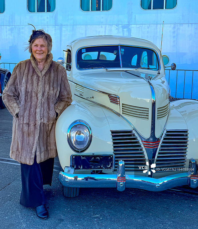穿着貂皮大衣的女人站在她的1939年经典汽车旁边图片素材