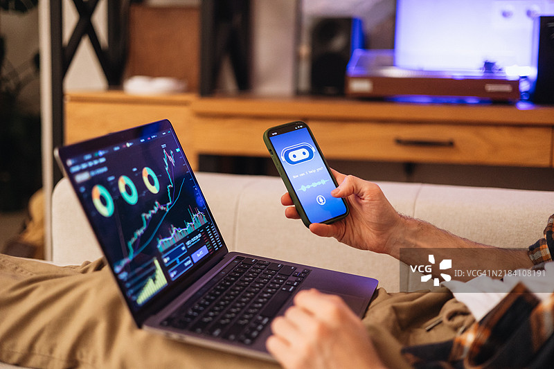 一个无法辨认的男子在手机应用上使用人工智能聊天机器人进行在线交易，同时在笔记本电脑上操作。图片素材