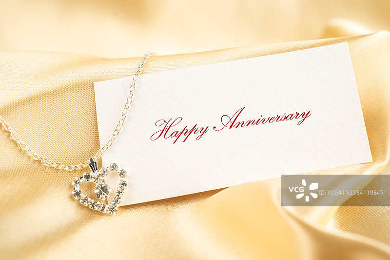黄色丝绸背景上的项链与快乐周年纪念标签纸。图片素材