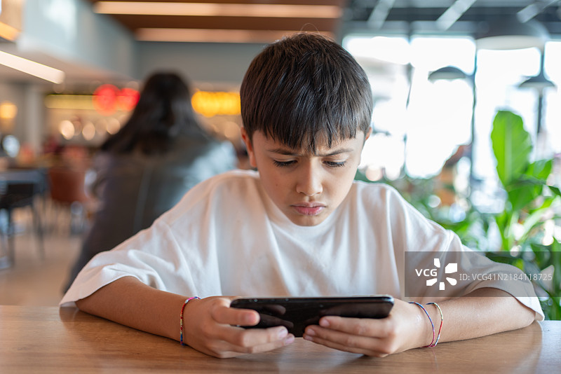 在餐厅里沉迷于手机游戏的男孩图片素材
