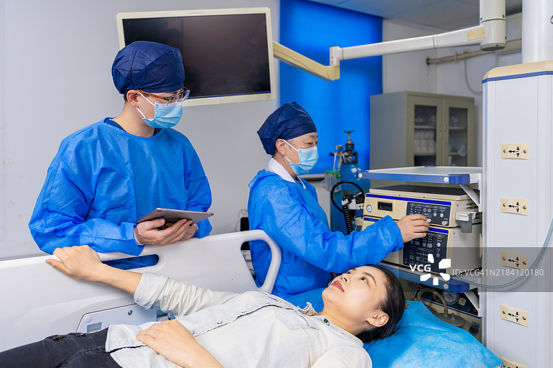亚洲女性胃肠病专家和男性护士在胃镜室使用数字平板与患者沟通治疗方案。图片素材