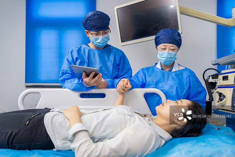 亚洲女性胃肠病专家和男性护士在胃镜室使用数字平板与患者沟通治疗方案。图片素材
