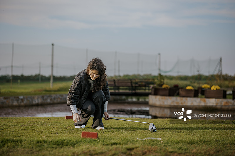 女性在阳光明媚的户外球场准备打高尔夫球图片素材