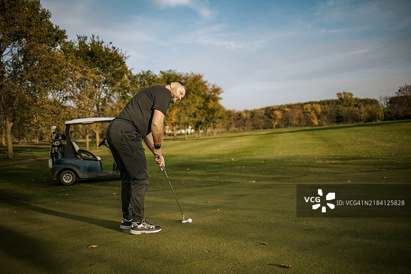 在阳光明媚的高尔夫球场上，一名男子正在用推杆打球。图片素材