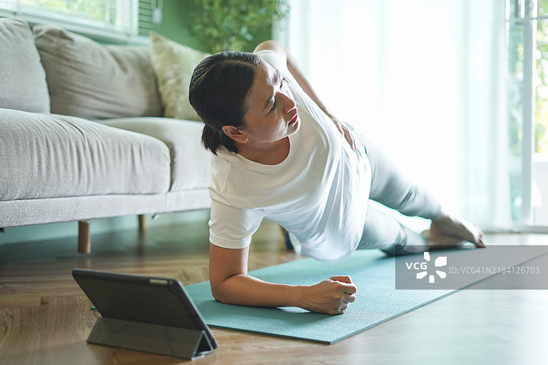 女人在瑜伽垫上锻炼，注视着平板电脑图片素材
