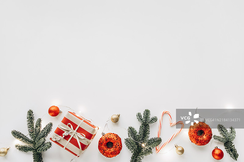 简约的圣诞平铺图，包含节日美食、包装礼物、糖果手杖心形和节日装饰品，背景为白色。温馨愉快的季节庆祝概念。图片素材