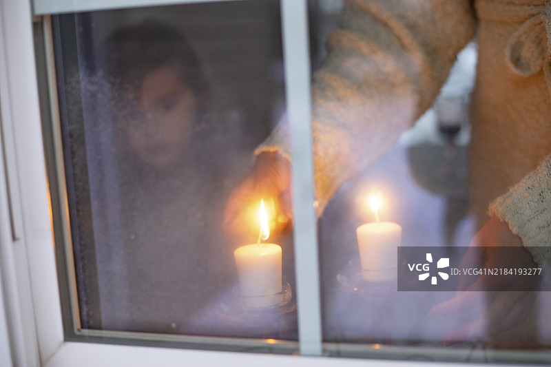 一个人在冰冷的窗边点燃蜡烛，营造出温馨的氛围，另一个人的倒影清晰可见。图片素材