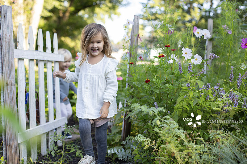微笑的孩子们在五彩缤纷的花园里玩耍，旁边是一道白色的栅栏。图片素材