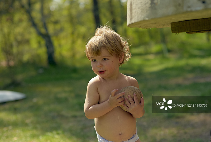 赤脚的小孩在户外阳光明媚的日子里，手里拿着一个球，背景是大自然。图片素材