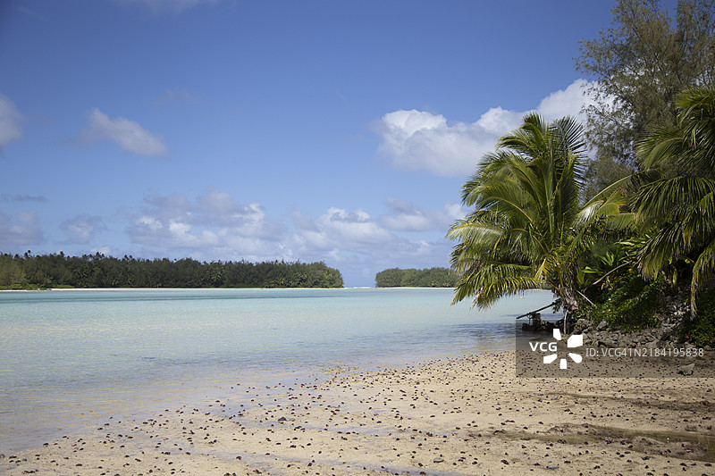宁静的热带海滩，清澈的蓝色海水、棕榈树和沙滩，在部分多云的天空下，位于库克群岛的拉罗汤加岛穆里。图片素材