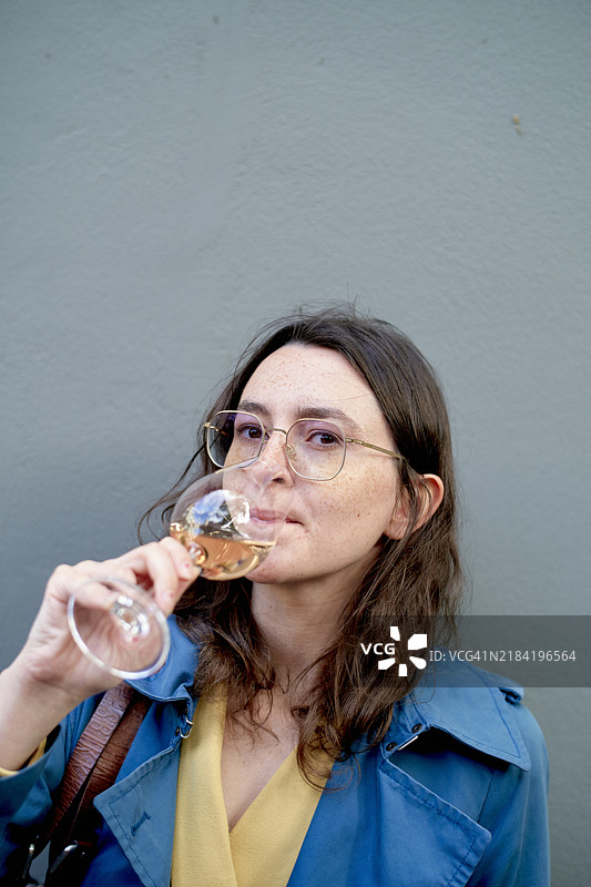 穿着蓝色外套的女性在灰色背景前品尝白葡萄酒图片素材